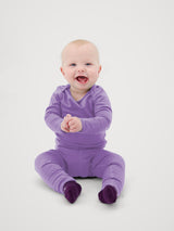 A happy baby wearing a purple Iksplor merino wool long sleeve shirt and matching pants with teal booties. #color_lilac