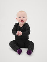 Iksplor baby wearing a black merino wool long sleeve shirt and pants with teal booties, sitting on a light background. #color_teton eclipse