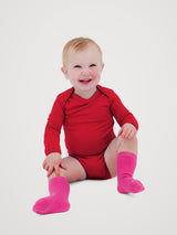 A smiling baby sitting on a light gray studio background, wearing a bright red long-sleeve bodysuit and hot pink knee-high socks. #color_campfire