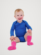 A smiling baby sitting on a light gray studio background, wearing a bright blue long-sleeve bodysuit and hot pink socks. #color_ocean