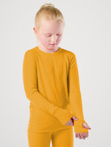 A young girl with blonde hair in a ponytail wearing a bright yellow long-sleeve shirt and matching yellow leggings, standing against a light gray studio background. #color_yellowstone