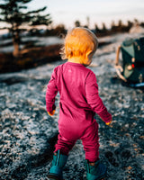 Toddler walking away on a rocky trail at sunset, wearing a deep pink Merino Wool Adventure Zippy romper and boots #color_peak pink