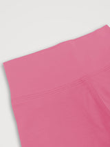 A close-up detail shot of a bright pink athletic garment, showing the waistband and seam stitching against a light gray background. #color_alpenglow
