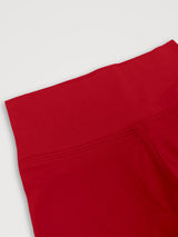 A close-up detail shot of bright red leggings showing the waistband and seam construction against a light gray background. #color_campfire