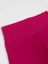 A close-up detail shot of bright red leggings showing the waistband and seam construction against a light gray background. #color_peak pink