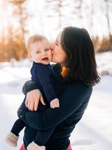 Iksplor baby wearing navy blue merino wool long sleeve shirt on a baby held by mother in a snowy outdoor setting #color_starry night