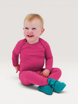 Iksplor baby wearing a bright pink merino wool long sleeve shirt and matching pants with teal booties. #color_peak pink