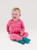 Iksplor baby wearing a pink merino wool long sleeve shirt and matching leggings with teal booties while sitting. #color_alpenglow