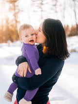 Mother kissing baby wearing a purple Iksplor merino wool long sleeve shirt outdoors in the snow . #color_lilac