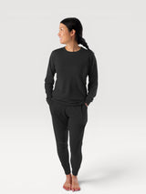 Woman wearing Iksplor black merino wool long-sleeve crew neck top and matching joggers in a studio setting. #color_teton eclipse