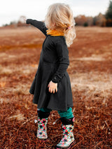 A young girl wearing a black Iksplor merino wool adventure dress with pockets, standing in a field. #color_teton eclipse - black