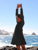 Girl wearing a black Iksplor merino wool adventure dress with arms raised outdoors by the ocean. #color_teton eclipse - black