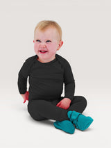 Iksplor baby wearing a black merino wool long sleeve shirt and pants with teal booties, sitting on a light background. #color_teton eclipse