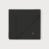 Iksplor Merino Wool Adventure Blanket in black, featuring a minimalist mountain logo, folded square. #color_teton eclipse