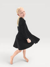 A young girl smiling while wearing a black Iksplor merino wool adventure dress with a flared skirt #color_teton eclipse - black