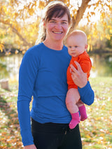 Iksplor blue merino wool nursing long sleeve top with thumb holes worn by a mother holding her baby outdoors. #color_ocean