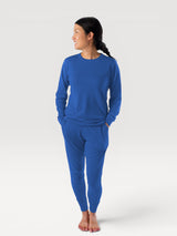 Woman wearing Iksplor blue merino wool long-sleeve crew neck top and matching joggers in a studio setting. #color_ocean