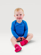 A smiling baby wearing a bright blue Iksplor merino wool long-sleeve bodysuit and pink booties. #color_ocean