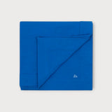 Iksplor blue merino wool adventure blanket folded neatly with a small embroidered mountain logo in the corner. #color_ocean