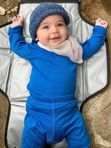 Iksplor baby wearing a bright blue merino wool bodysuit and matching pants with a knit hat and striped bib #color_ocean
