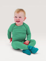 Iksplor baby wearing a green merino wool long sleeve shirt and matching pants with fold-over mitts sitting on floor #color_meadow