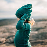 Child wearing a soft green Iksplor merino wool beanie outdoors in a natural setting #color_evergreen