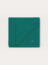 Iksplor green merino wool adventure blanket folded square with a small embroidered mountain logo in the corner. #color_evergreen