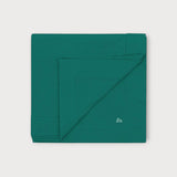 Iksplor green merino wool adventure blanket folded square with a small embroidered mountain logo in the corner. #color_evergreen
