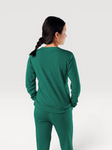 Woman wearing an Iksplor green merino wool adventure crew long sleeve shirt, back view #color_evergreen