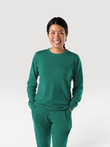Woman wearing an Iksplor green merino wool long-sleeve crew neck adventure top with a comfortable fit. #color_evergreen