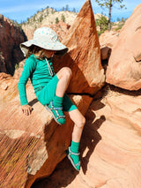 Child wearing Iksplor green merino wool blend trail socks with sandals while hiking on red desert rocks #color_jungle trek