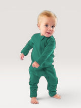 A baby wearing an Iksplor green merino wool zip romper with long sleeves and snug cuffs, standing against a grey background. #color_evergreen