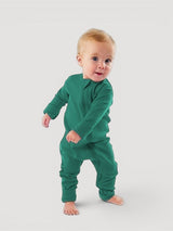 A baby wearing an Iksplor green merino wool zip romper with long sleeves and snug cuffs, standing against a grey background. #color_evergreen