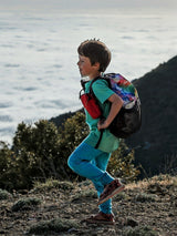 Child wearing Iksplor blue merino wool joggers and green t-shirt hiking on a mountain trail with a colorful backpack. #color_meadow