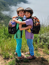 Two happy children wearing Iksplor merino wool joggers and t-shirts while hiking outdoors with backpacks. #color_meadow