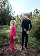 Iksplor kids merino wool long sleeve tops in pink and navy worn by children playing in a forest setting #color_peak pink