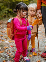 Iksplor kids merino wool long sleeve top in bright pink worn by a toddler hiking in the forest with a backpack. #color_peak pink