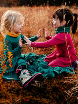 Two young girls playing on an Iksplor Merino Wool Adventure Blanket in a grassy field during autumn. #color_peak pink