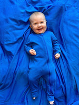 A smiling baby wearing a royal blue onesie lying on a matching Iksplor Merino Wool Adventure Blanket. #color_ocean