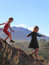 Two girls wearing Iksplor merino wool adventure dresses hiking on a rocky mountain trail in the sunshine. #color_teton eclipse - black