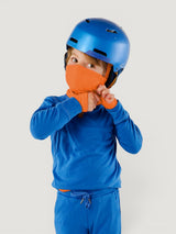 Child wearing an orange Iksplor merino wool balaclava under a blue helmet, showing full face and neck coverage. #color_poppy