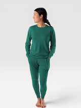 Woman wearing an Iksplor green merino wool long-sleeve crew neck top and matching joggers for outdoor adventure. #color_evergreen