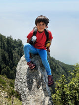Child wearing Iksplor blue merino wool jogger pants and red t-shirt, sitting on a mountain rock while hiking. #color_campfire