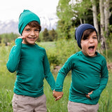 Two boys wearing Iksplor merino wool beanies in green and navy while holding hands in a grassy field.
