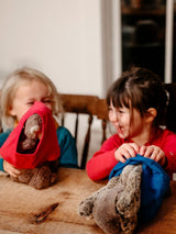 Two children playing with plush toys while wearing Iksplor merino wool underwear as hats at a wooden table. #color_ocean