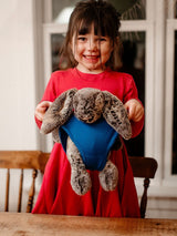 A smiling girl wearing a red dress holds a plush bunny wearing blue Iksplor merino wool underwear. #color_ocean