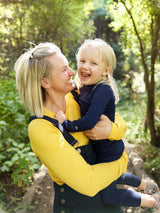 Iksplor merino wool long sleeve top worn by a child in navy blue while being held by a woman in a yellow top #color_yellowstone