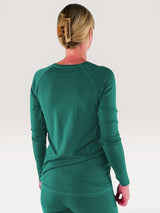 Back view of a woman wearing an Iksplor long sleeve merino wool nursing top in forest green with thumb holes. #color_evergreen