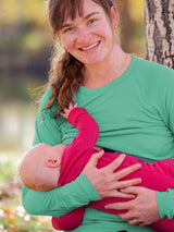 Iksplor merino wool nursing top in green with thumb holes, worn by a mother breastfeeding her baby outdoors. #color_meadow