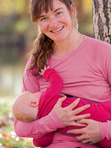 A mother wearing a dusty rose Iksplor merino wool nursing top with thumb holes while breastfeeding her baby outdoors. #color_alpenglow